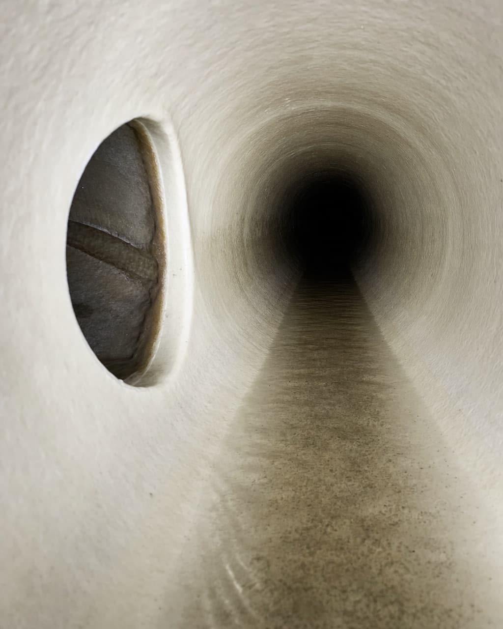 A reinstated lateral connection seen from inside a lined main pipe, the opening cut cleanly through the resin liner