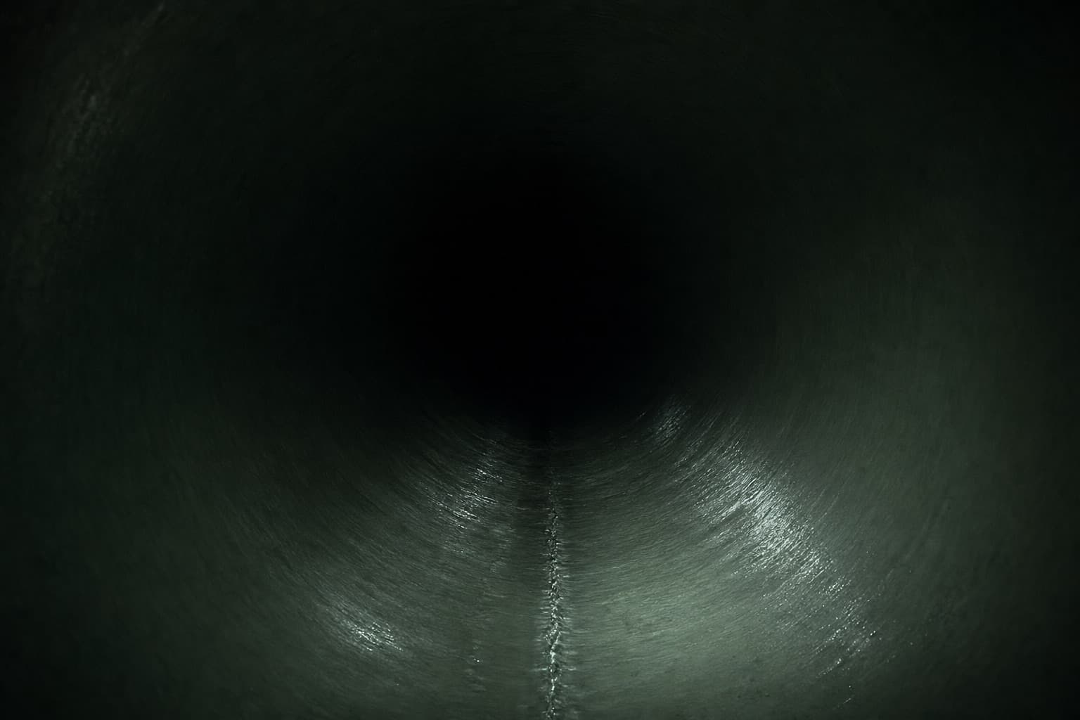 The inside of a large pipe with a freshly cured resin liner, lit by a single beam receding into blackness